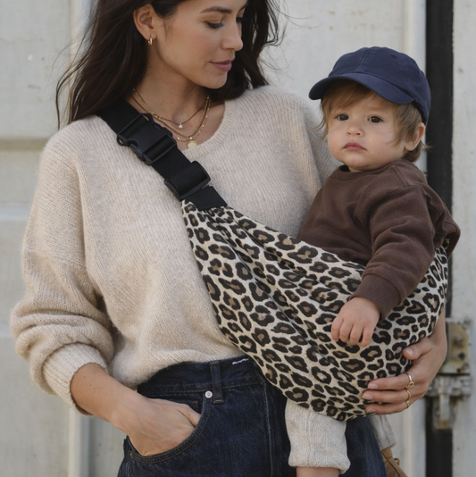 maman brune qui porte son bébé dans un sling leopard, portage hanche. bébé dans une position physiologique