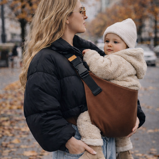 Maman tient son bébé dans un porte-bébé sling marron portage hanche, epaules et dos soulagé de la mère
