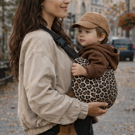 maman portant son enfant en position M dans un porte bebe sling portage hanche en ville en automne