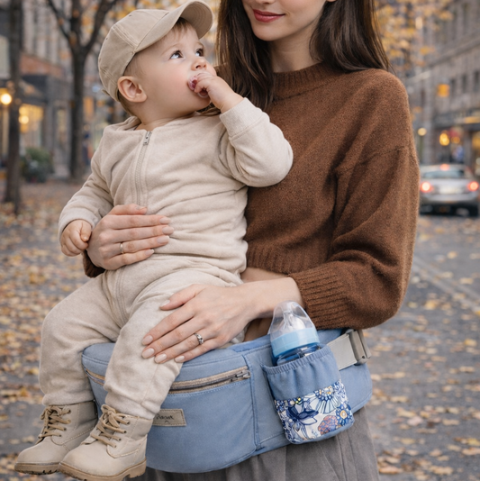 maman qui porte son bébé dans un porte-bébé multi position bleu, en ville. la maman le tient pour qu'il soit maintenu