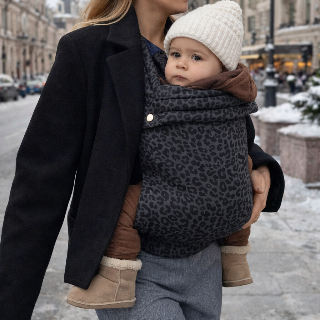 Porte-bébé physiologique motifs Léopard, maman blonde, veste noire et bébé avec bonnet beige dans portage position M