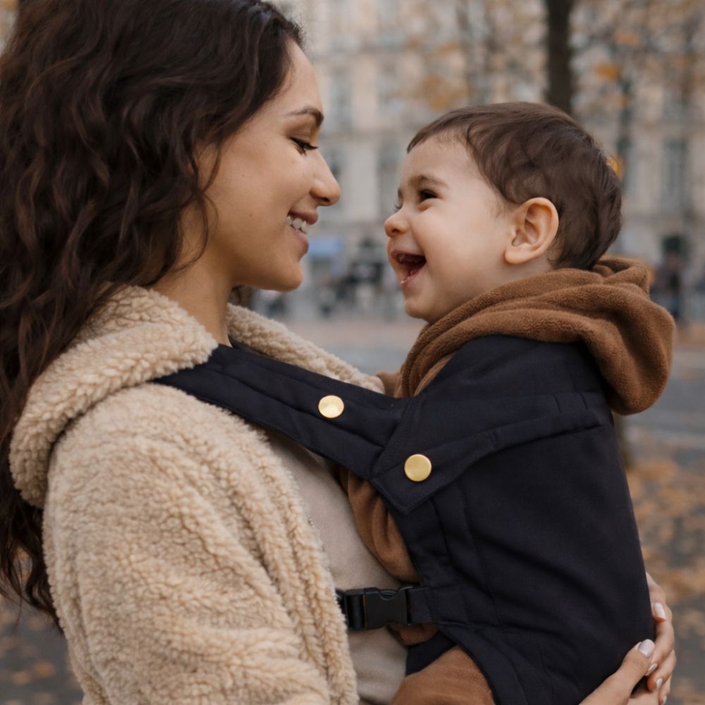 Maman sourie à son bébé, il est dans son porte bébé kangourou, la position physiologique est respectée, coloris noir