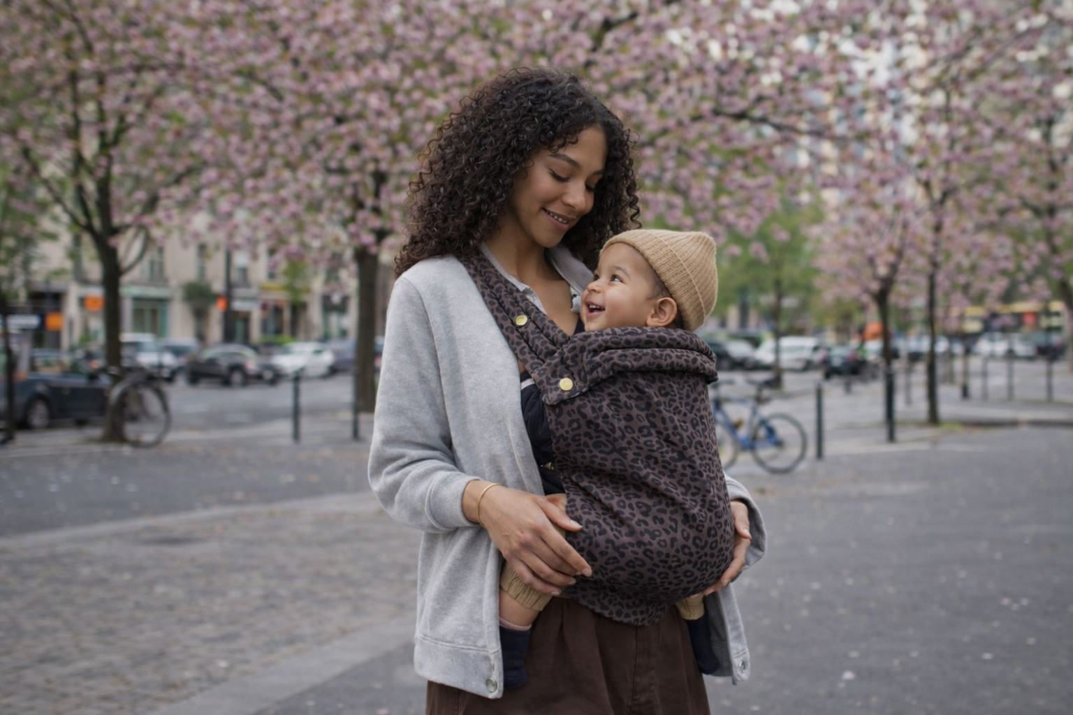 Maman qui porte son bébé dans un porte-bébé leopard kangourou ergonomique, le bébé est bien maintenu en position M