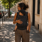 Maman brune qui porte son bébé dans un porte-bébé kangourou léopard gris dans la rue en été