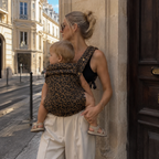 Maman blonde qui porte son bébé dans un porte-bébé kangourou léopard café dans la rue au printemps