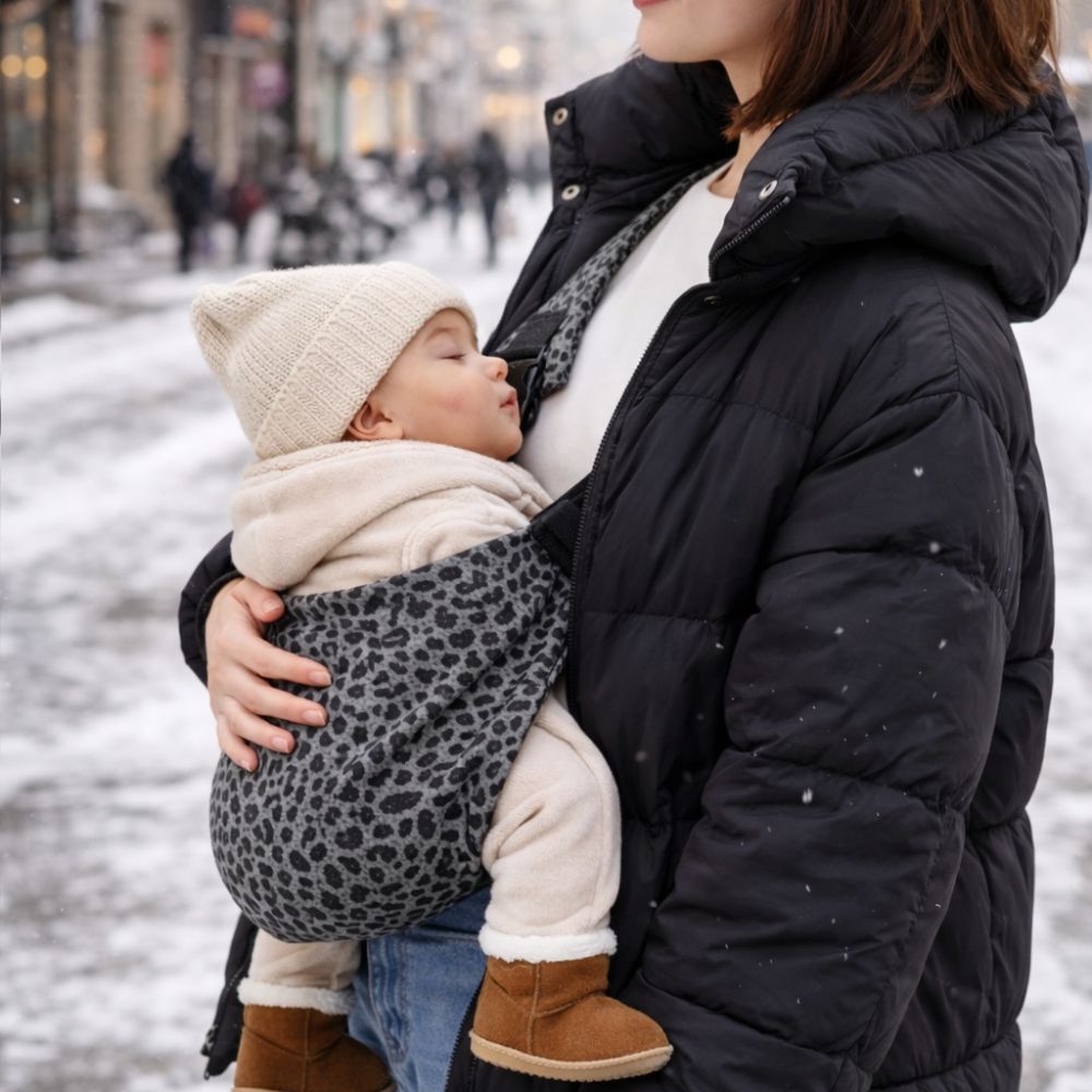 Maman qui tient son bébé dans un porte bébé coloris léopard anthracite. Bébé est apaisé, ville hiver