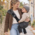 Maman blonde avec une veste moumoute qui tient son enfant dans un sling léopard gris