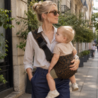 maman blonde qui porte son bébé dans la rue au printemps avec un sling leopard café