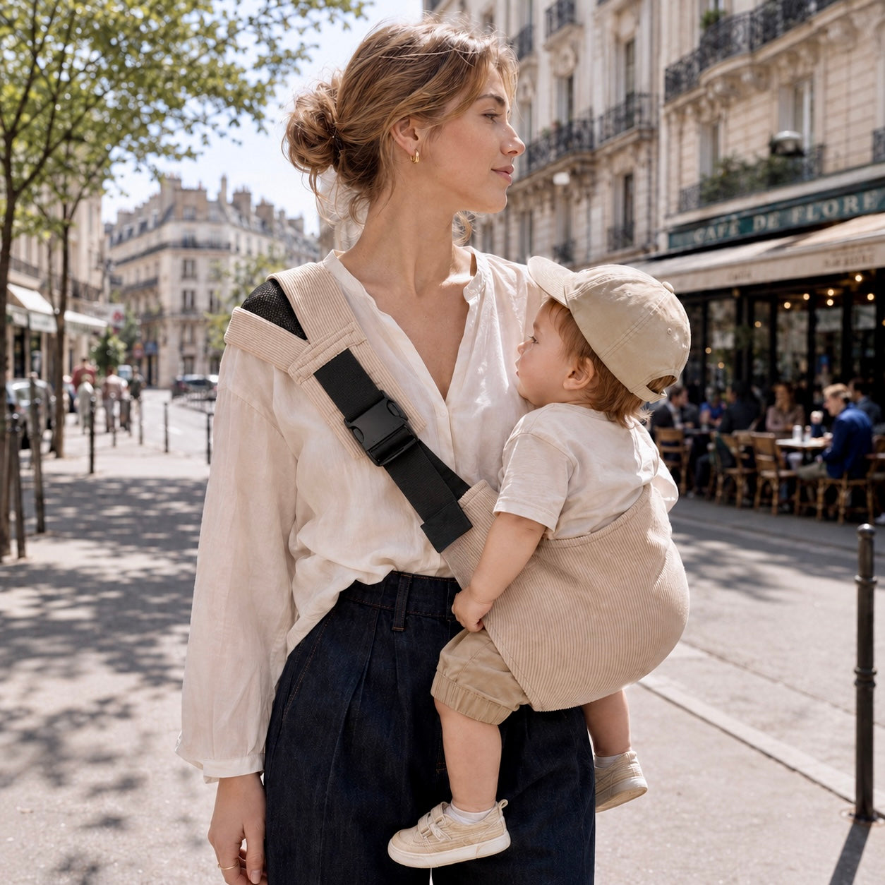 Maman chatain clair porte son bébé dans un sling portage hanche beige en velours côtélé. C'est tellement pratique