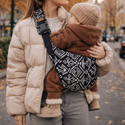 Porte-bébé style sling avec portage physio, bébé porté latéral par sa maman en ville. Motifs aztek coloris noir. Bébé en position physiologique