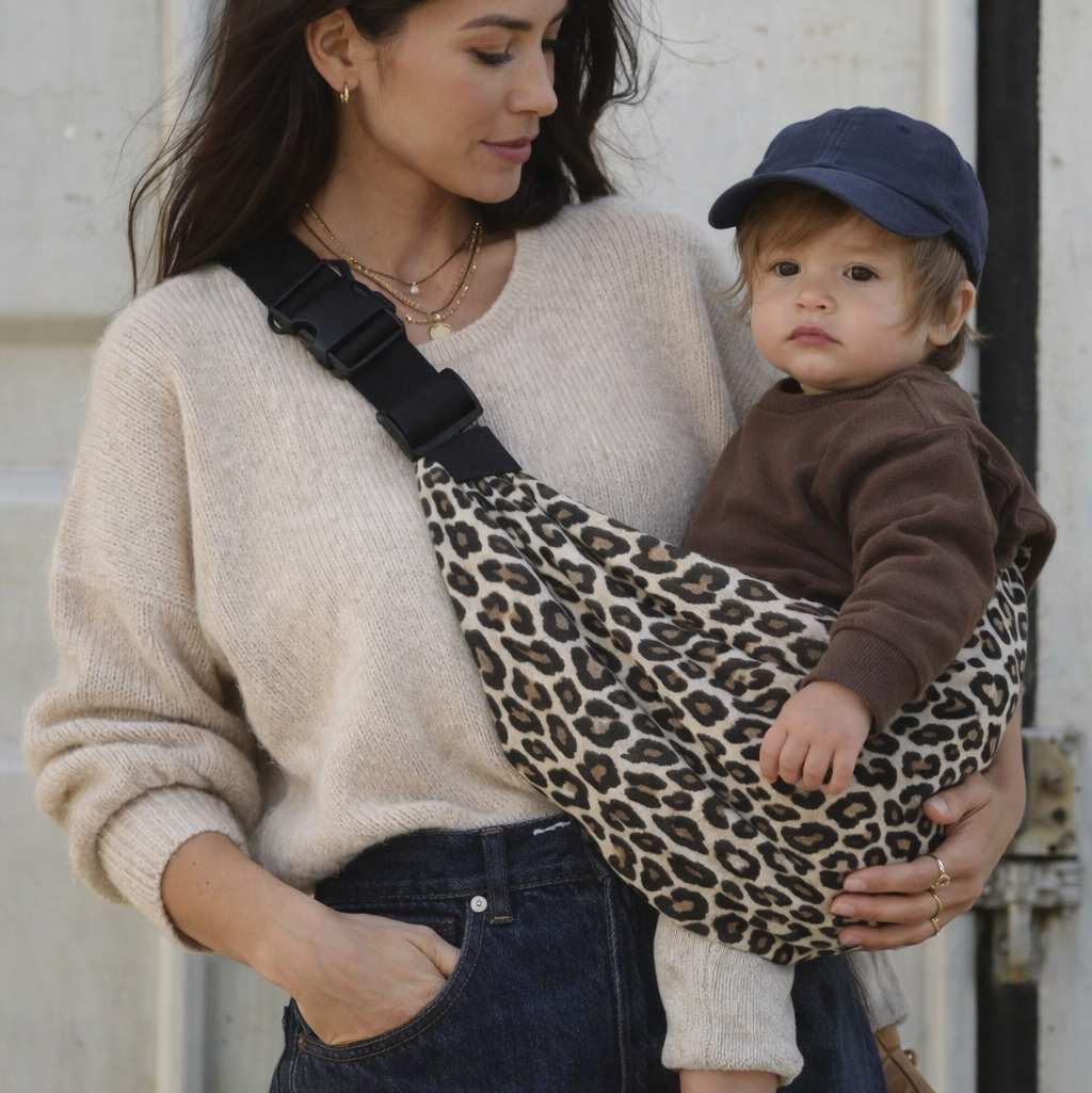 maman brune qui porte son bébé dans un sling leopard, portage hanche. bébé dans une position physiologique