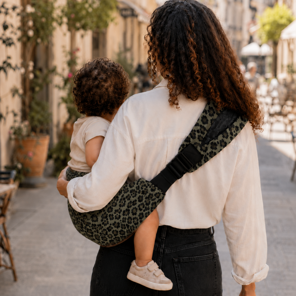 Maman métisse de dos se balade avec son fils dans la rue. Elle le tient dans un porte bébé léopard olive