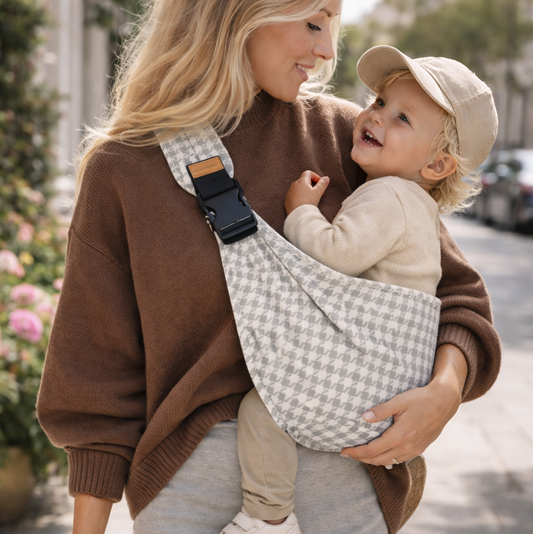 Maman qui porte son bébé dans un sling pied-de-poule. bébé est apaisé avec un portage hanche