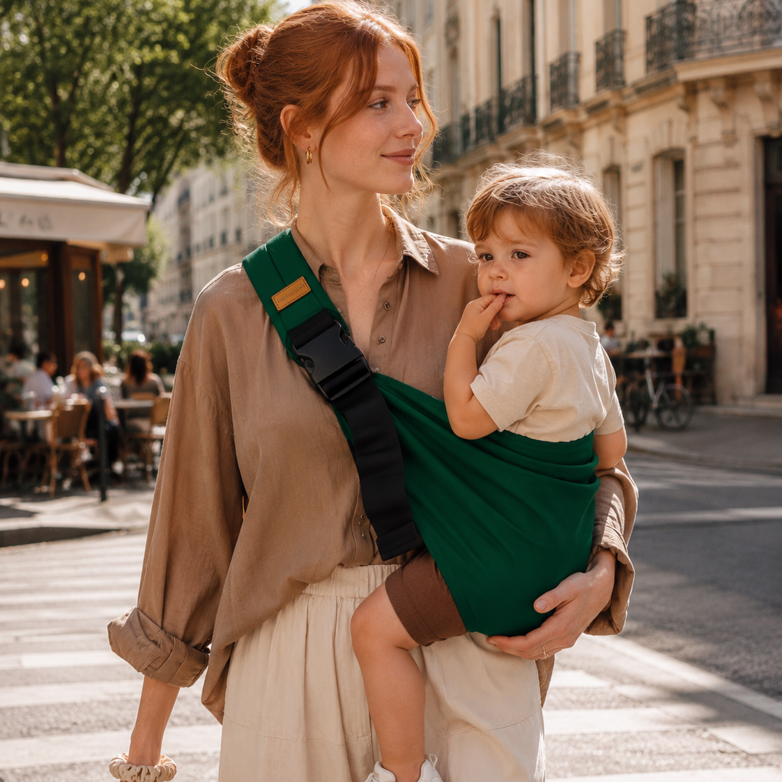 Maman rousse porte son enfant dans la rue. il est bien installé dans ce porte-bébé sling vert