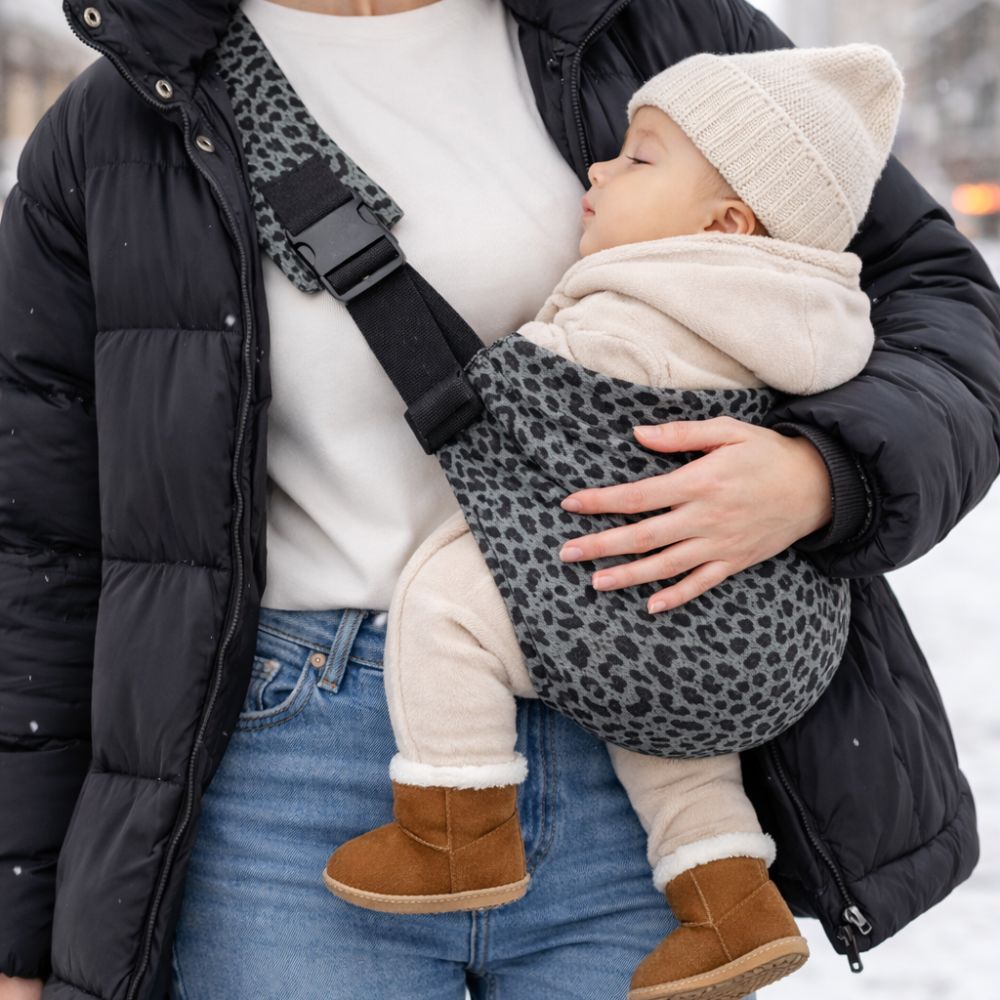 Maman porte son bébé apaisé dans un porte bébé latéral sling motif leopard gris, en ville hiver