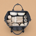 Sac à dos à langer gris sur un fond beige nuancier vue de l'intèrieur avec l'essentiel pour bébé
