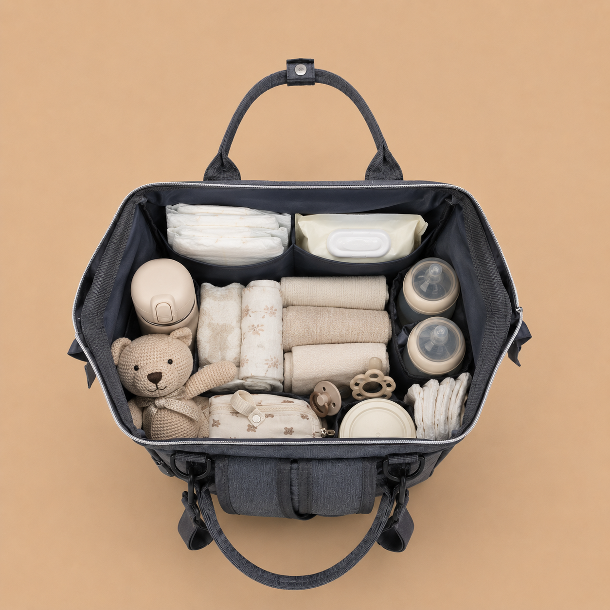 Sac à dos à langer gris sur un fond beige nuancier vue de l'intèrieur avec l'essentiel pour bébé