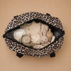 Sac à langer bébé coloris léopard sur fond  beige, vue de l'intérieur avec l'essentiel de bébé. Pratique, confortable et stylé pour le quotidien