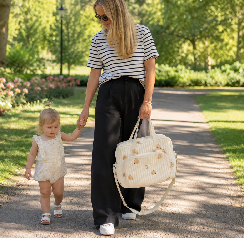 Maman blonde qui se balade avec son sac à langer motif ourson au parc avec sa petite fille